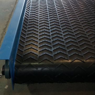 Chevron cleat rubber conveyor belt wrapped around a pulley on a blue steel frame
