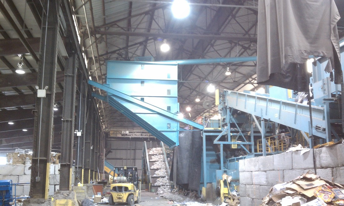 Elevated silo storage bin over a baler feed conveyor, leaving drive-thru access below