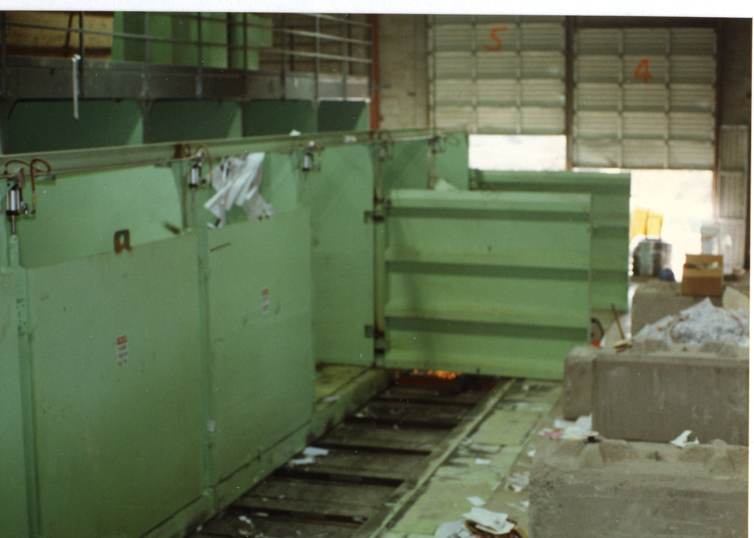 Heavy-duty bunker walls with doors that discharge onto an in-ground baler feed conveyor
