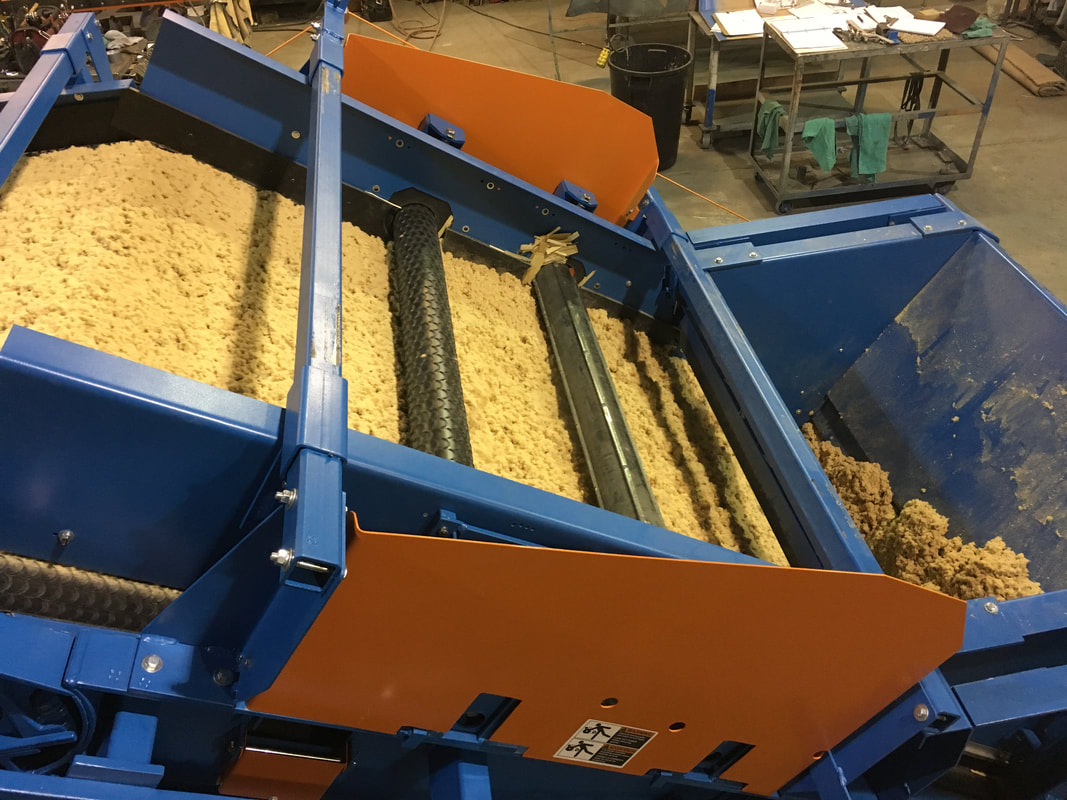 Side view of the inclined conveyor section with sawdust being leveled by two leveling rollers above the belt