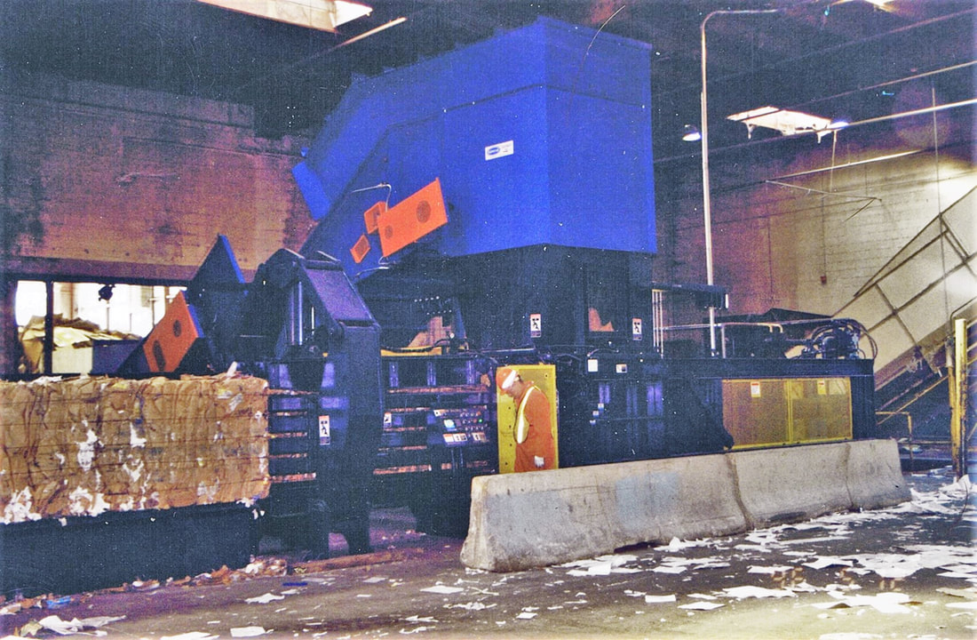 Above-ground low-profile slider bed conveyor with elbow-up feeding the hooded baler feed conveyor