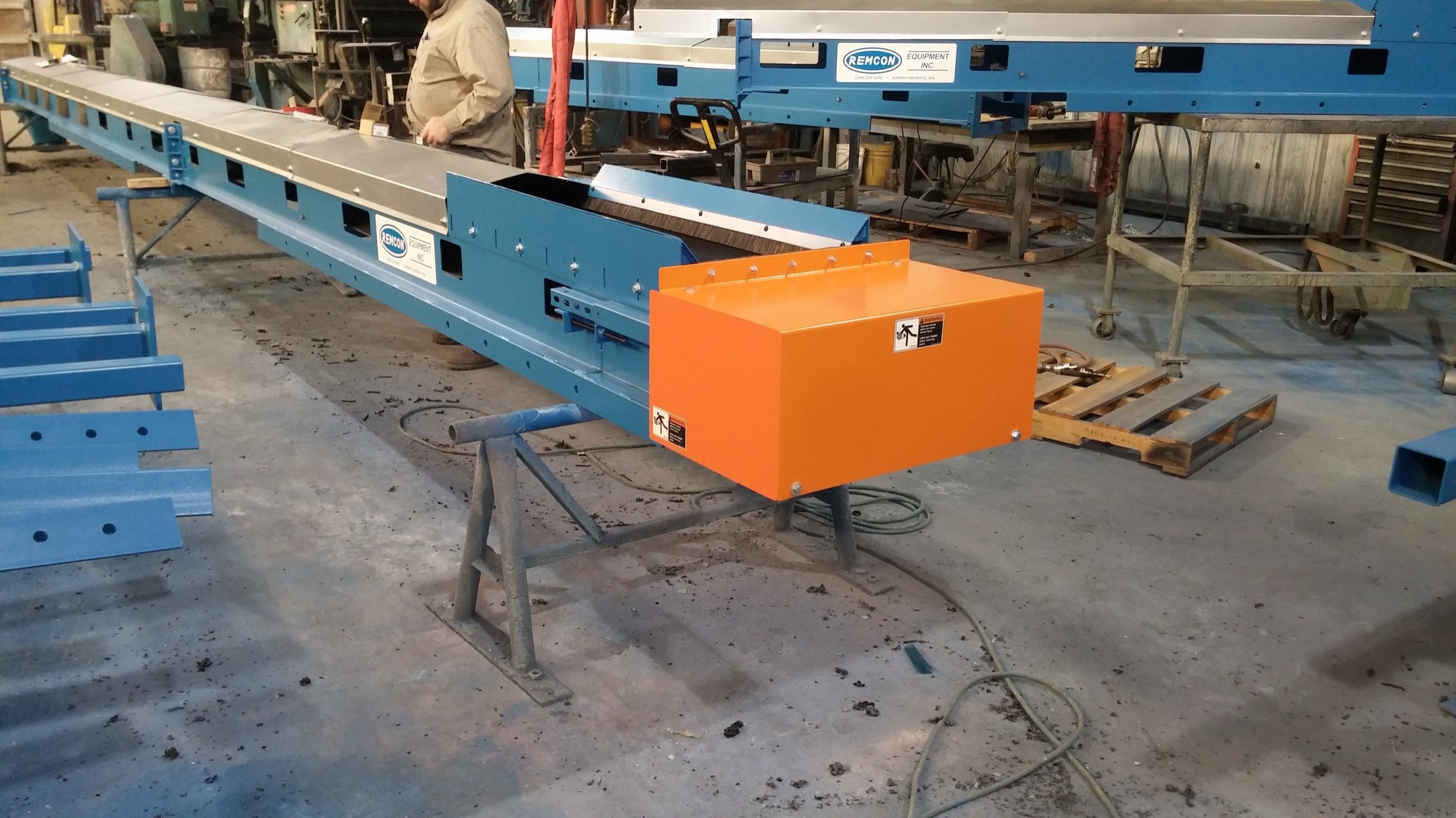 A Remcon conveyor being fabricated in the shop, with raw structural steel members and a worker in the background