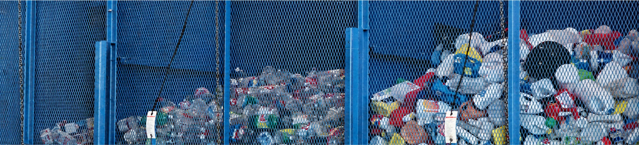 Separated plastic bottles, cans, and containers held in blue mesh storage bunkers at a recycling facility