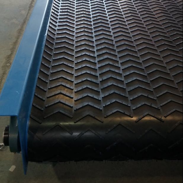 Transfer conveyor with chevron rubber belt cleats